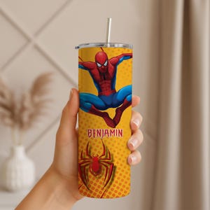 May include: A yellow tumbler featuring the superhero Spider-Man in a dynamic pose. The tumbler has a red and black Spider-Man logo and the name "BENJAMIN" in red. It includes a silver straw and a yellow lid.