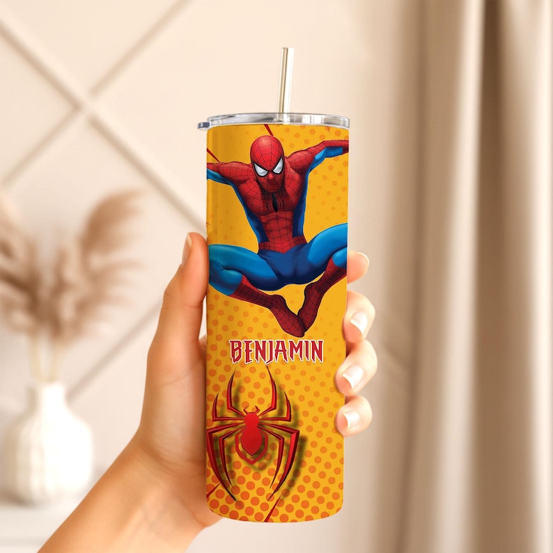 May include: A yellow tumbler featuring a Spider-Man design. The tumbler has a red and blue Spider-Man graphic, the name "BENJAMIN", and a red spider logo. It includes a straw.
