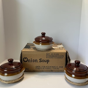 May include: Three stoneware onion soup bowls with dark brown lids and cream-colored bases, each resting on a woven rattan basket. The original cardboard box is present, featuring the text "Onion Soup" and "Set of four stoneware soups with rattan basket."