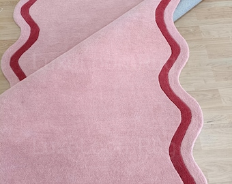 May include: Two pink, wavy-edged rugs with a dark red border. One rug is partially rolled up, revealing a gray backing. The rugs are on a light wood floor. The rugs have a soft, plush texture.