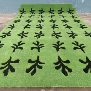 May include: A rectangular green rug with a repeating black leaf pattern. The rug is made of a soft material and has a thick pile. The rug is rolled up at the top.