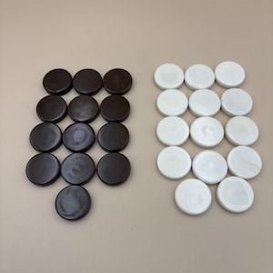 May include: A collection of twenty-four round game pieces. Twelve are dark brown, and twelve are white. The pieces are arranged in two groups on a neutral background. The game pieces are likely for a board game like checkers or backgammon.