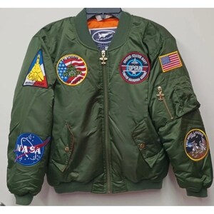 Puede incluir: Chaqueta bomber verde con múltiples parches bordados, incluyendo un logo de la NASA, una bandera estadounidense y un parche "Top Gun". La chaqueta tiene cierre de cremallera y dos bolsillos delanteros. La chaqueta es talla mediana.