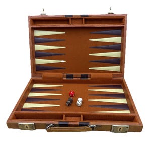 Może przedstawiać: Otwarty brązowy skórzany zestaw do backgammona z filcową powierzchnią do gry. Zestaw zawiera kostki do gry i uchwyt do przenoszenia. Plansza do gry ma brązowe, złote i czarne trójkąty.