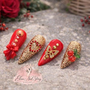 Könnte beinhalten: Vier rote und goldene Nageldesigns. Ein Nagel zeigt eine rote Schleife, ein anderer ein Herz aus roten Edelsteinen, ein dritter einen goldenen Schmetterling und der letzte rote Kirschen. Die Nägel sind mit goldenem Glitzer und Edelsteinen verziert.