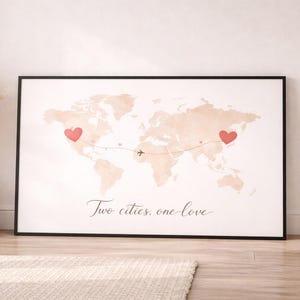 Könnte beinhalten: Gerahmter Weltkarten-Druck mit Aquarell-Effekt in neutralen Tönen. Zwei rote Herzen markieren Orte, verbunden durch eine gestrichelte Linie und ein Flugzeugsymbol. Der Text "Two cities, one love" ist kursiv geschrieben.