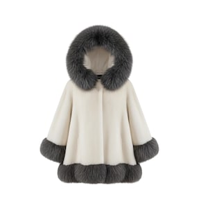 May include: A cream-coloured cape with a hood and fur trim. The hood and cuffs are trimmed with dark grey fur. The cape has a button closure down the front and is designed to be worn over the shoulders.