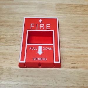 May include: A red fire alarm pull station with white lettering and a white border. The word "FIRE" is at the top, with "PULL DOWN" and an arrow in the middle. The brand "SIEMENS" is at the bottom.