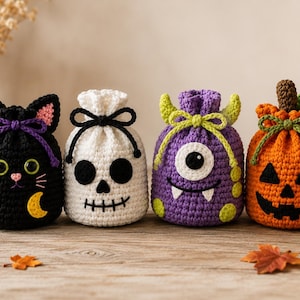 Könnte beinhalten: Vier gehäkelte Beutel mit Kordelzug im Halloween-Design: eine schwarze Katze mit gelbem Mond, ein weißer Totenkopf, ein violettes einäugiges Monster mit Hörnern und ein orangefarbener Kürbis mit braunem Stiel und grünen Blättern.