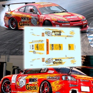 May include: A decal sheet featuring yellow and black graphics for a model car, including HKS and Genki logos, flame patterns, and a cartoon face. The sheet is displayed over images of a red drift car with matching livery and sponsor decals.
