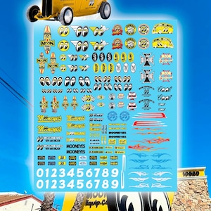 May include: A yellow hot rod car and a sheet of decals featuring various designs, including the "MOONEYES" logo, racing flags, and eye graphics. The decals also include numbers and flames.