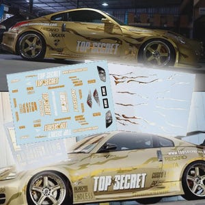 Puede incluir: Un coche deportivo dorado con el texto "TOP SECRET" y varios logotipos de marcas. El coche tiene llantas personalizadas y un diseño de pintura único. También se incluyen hojas de calcomanías con logotipos y texto adicionales.