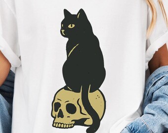 Camiseta com estampa de gato preto sobre caveira, estilo gótico/terror.