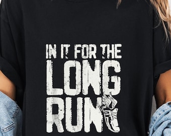 May include: Black t-shirt with the text "IN IT FOR THE LONG RUN" in white, distressed font. A white graphic of a running shoe is below the text. The shirt is worn with a denim jacket and shorts.