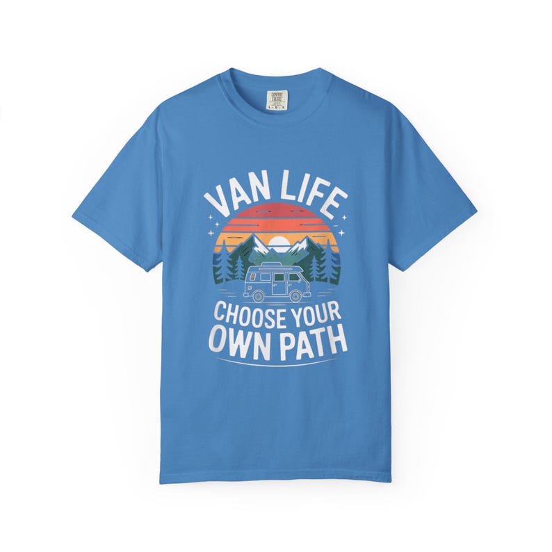 May include: A light blue t-shirt with the words "VAN LIFE" above a graphic of a van, mountains, and trees. Below the graphic, the text reads "CHOOSE YOUR OWN PATH". The design features a sunset color scheme.