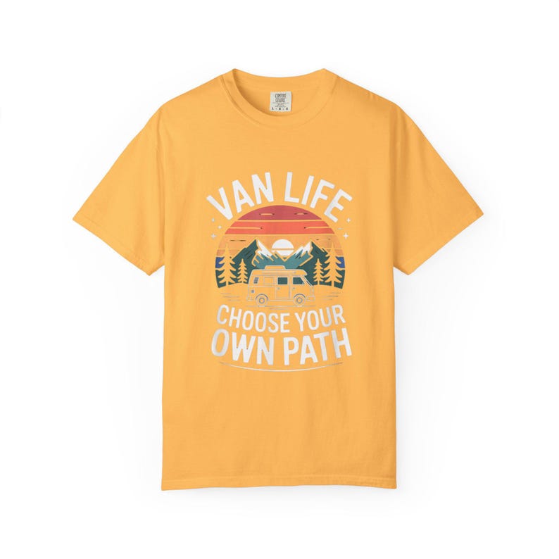 May include: Mustard yellow t-shirt with a graphic design. The design features the words "VAN LIFE" above a sunset scene with a camper van, mountains, and trees. Below the scene, the text reads "CHOOSE YOUR OWN PATH."