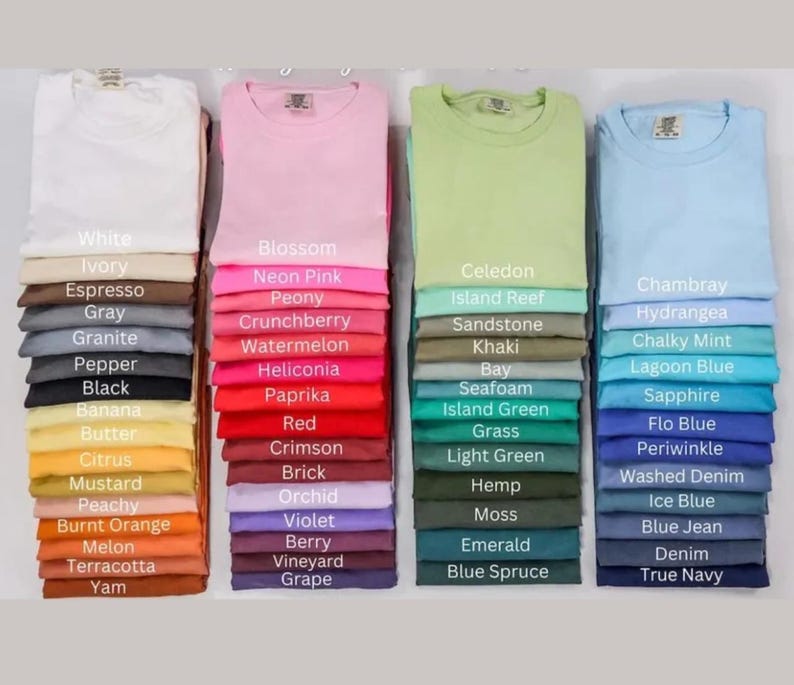 May include: A display of folded t-shirts in various colors, including white, pink, green, and blue. Each stack is labeled with the color name, such as "Blossom," "Celedon," and "Chambray." The shirts are neatly arranged, showcasing a range of hues.