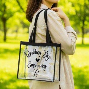 Puede incluir: Un bolso tote de plástico transparente con bordes y asas negras. La parte frontal del bolso presenta el texto impreso en negro Wedding Day Emergency Kit con un pequeño icono de corazón negro centrado entre las palabras Wedding Day y Emergency Kit.