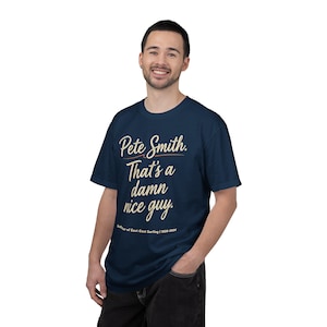 Op de afbeelding: Marineblauw t-shirt met de tekst "Pete Smith. That's a damn nice guy." in cursief schrift. Het shirt bevat ook de tekst "Godfather of East Coast Surfing / 1930-2024".
