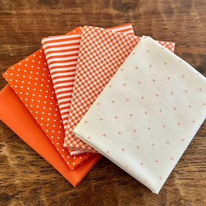 May include: A collection of orange fabric squares with various patterns, including polka dots, stripes, gingham, and a cream-colored fabric with small red crosses. The fabrics are neatly arranged, showcasing a variety of textures and designs.