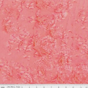 May include: Coral-colored fabric with a batik-style pattern. The fabric features a mottled design with lighter and darker shades of coral and peach, creating a textured appearance. The fabric is marked with a ruler in inches.