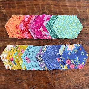 May include: A collection of fabric hexagons arranged in two horizontal rows. The top row features shades of orange, pink, and green, while the bottom row displays yellow, blue, and floral patterns. Each piece has pinked edges and a variety of prints.