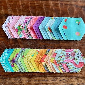 May include: A collection of fabric hexagons arranged in two horizontal rows. The pieces feature a variety of colors including pink, purple, teal, yellow, and orange, with patterns such as floral prints, geometric shapes, and a flamingo illustration.