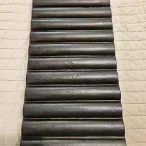 May include: A dark gray cast iron loaf pan with a ribbed design. The pan has a handle on one end and the number "154" is visible. The pan is designed for baking bread or other baked goods.