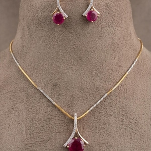 May include: A jewelry set featuring a necklace and matching earrings. The necklace has a gold and silver chain with a pendant featuring a large, round, red gemstone. The earrings have a similar design with red gemstones and diamond accents.