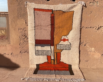 May include: A rectangular, abstract rug with a geometric design. The rug features a cream-colored background with sections of orange, red, brown, and black. The design includes vertical and horizontal shapes, creating a modern, artistic look.
