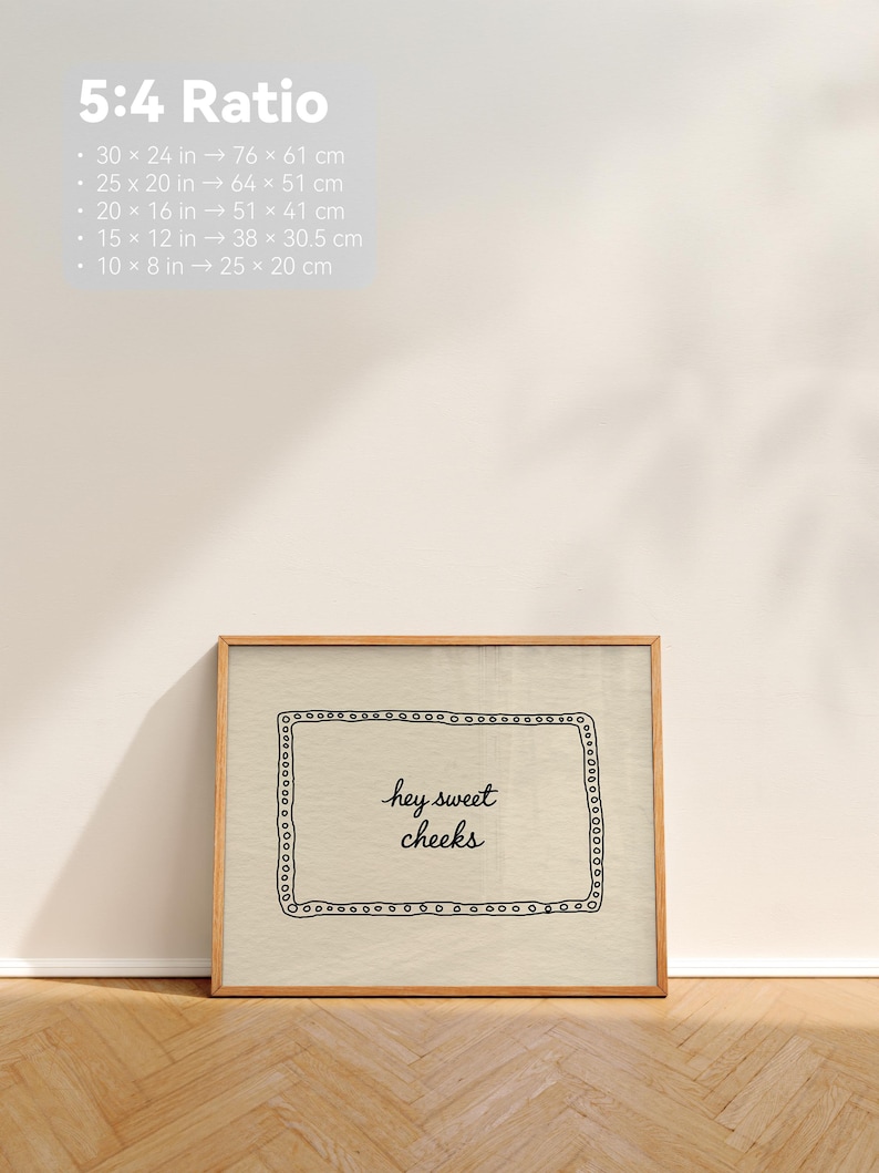 May include: A framed print with the text "hey sweet cheeks" in a handwritten style. The print is in a wooden frame and has a beige background. The image also includes size conversions in inches and centimeters.