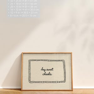 May include: A framed print with the text "hey sweet cheeks" in a handwritten style. The print is in a wooden frame and is leaning against a white wall. The frame dimensions are 32 x 24 inches (81 x 61 cm), 24 x 18 inches (61 x 46 cm), 20 x 15 inches (51 x 38 cm), 16 x 12 inches (41 x 30.5 cm), 12 x 9 inches (30.5 x 23 cm), and 8 x 6 inches (20.5 x 15 cm).