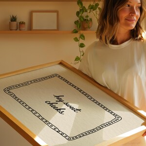May include: A framed canvas print with the text "hey sweet cheeks" in a handwritten style. The print has a light-colored background with a black border of small circles. The frame is made of light-colored wood.