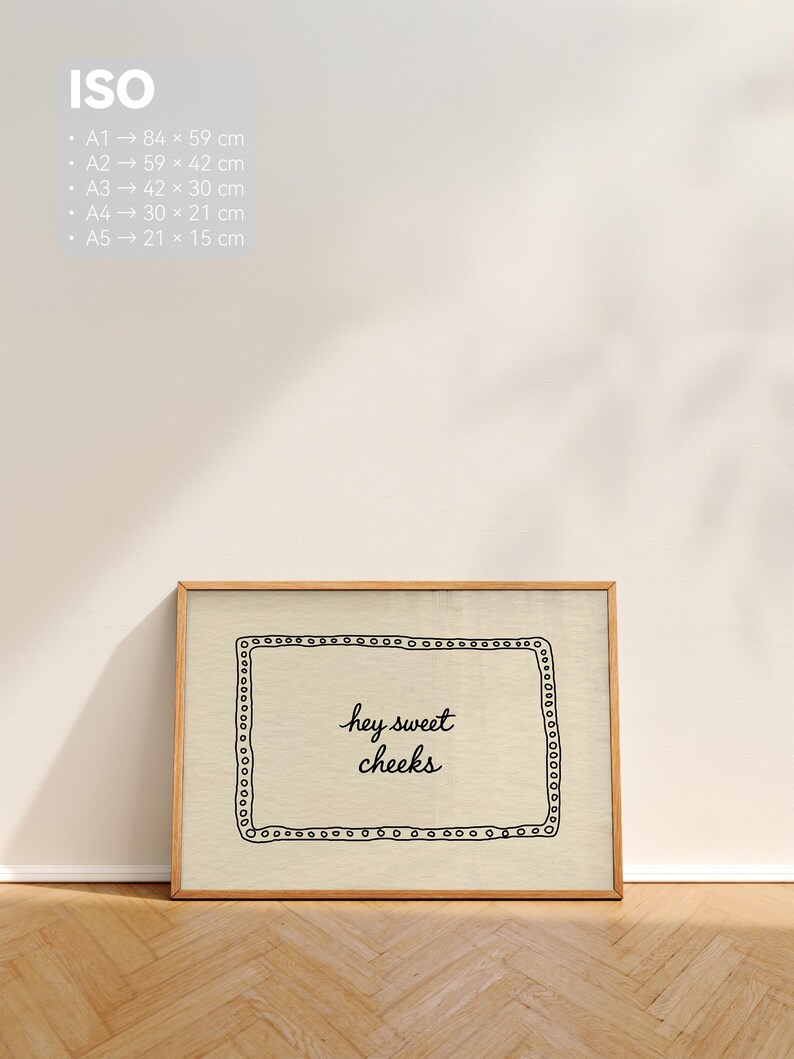 May include: A framed print with the text "hey sweet cheeks" in a handwritten style. The print has a light beige background with a black border of small circles and a wooden frame. The print sizes are listed in centimeters.