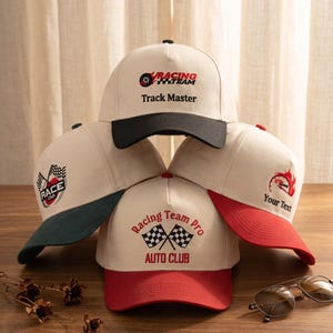 May include: Five beige baseball caps with different colored brims. Each cap has a racing-themed logo and text, including "Track Master," "Race Car," and "Racing Team Pro Auto Club." One cap has "Your Text" printed on it.