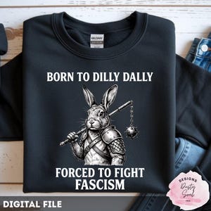 May include: Black sweatshirt with the text "BORN TO DILLY DALLY" above a rabbit illustration holding a mace, and "FORCED TO FIGHT FASCISM" below. The design is a digital file.