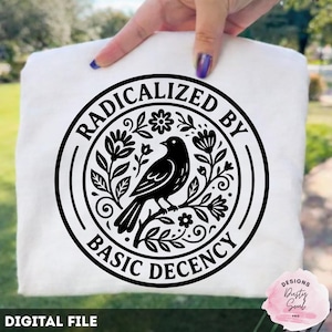 Op de afbeelding: Een wit t-shirt met een zwart cirkelvormig ontwerp. Het ontwerp toont een vogel op een tak, omringd door bloemen en bladeren. De tekst "RADICALIZED BY BASIC DECENCY" staat rond het ontwerp. De tekst "DIGITAL FILE" staat onderaan.