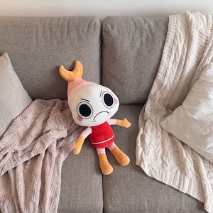 Puede incluir: Un peluche con forma de camar&oacute;n que presenta una cabeza blanca grande, ojos negros circulares y una boca fruncida. Tiene una cola rosa y naranja, un torso rojo, brazos de color rosa claro y piernas naranjas. Posee peque&ntilde;os c&iacute;rculos rosas en las mejillas.