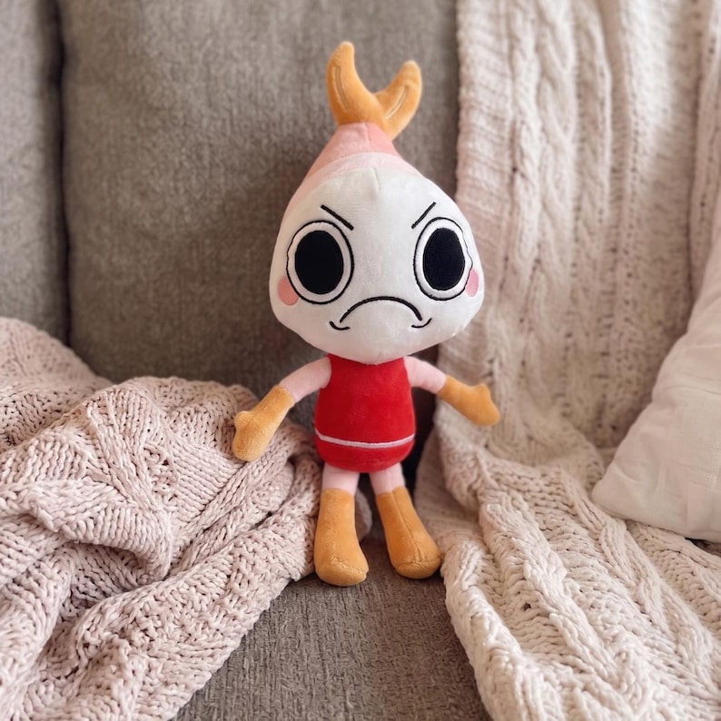 Puede incluir: Un peluche con forma de gamba que tiene la cabeza blanca, grandes ojos negros y una boca fruncida. Presenta una parte superior rosa, un cuerpo rojo con una fina l&iacute;nea horizontal blanca, y brazos y piernas de color naranja claro.
