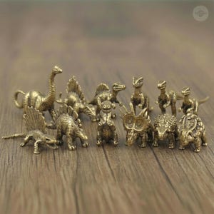 May include: A collection of eleven miniature brass dinosaur figurines, each featuring detailed textures and a metallic gold finish. The set includes various species such as a long-necked sauropod, several armored dinosaurs, and bipedal predators.