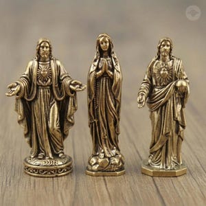 Puede incluir: Tres estatuas religiosas de bronce. La estatua de la izquierda representa una figura con los brazos extendidos, la estatua central muestra una figura con las manos juntas en oraci&oacute;n y la estatua de la derecha representa una figura sosteniendo un globo.