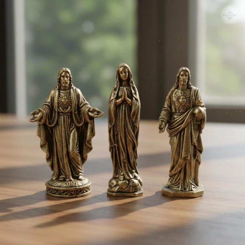 Puede incluir: Tres figuras religiosas de bronce. La figura central es una estatua de una mujer con las manos juntas en oraci&oacute;n. Las otras dos figuras son de un hombre con los brazos extendidos y un hombre sosteniendo un globo. Las figuras est&aacute;n sobre una superficie de madera.