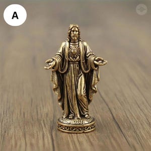 Puede incluir: Una estatua de bronce de Jesucristo con los brazos extendidos. La figura est&aacute; representada con t&uacute;nicas fluidas, con un rostro detallado y un dise&ntilde;o de sol en el pecho. La estatua est&aacute; montada sobre una base decorativa.