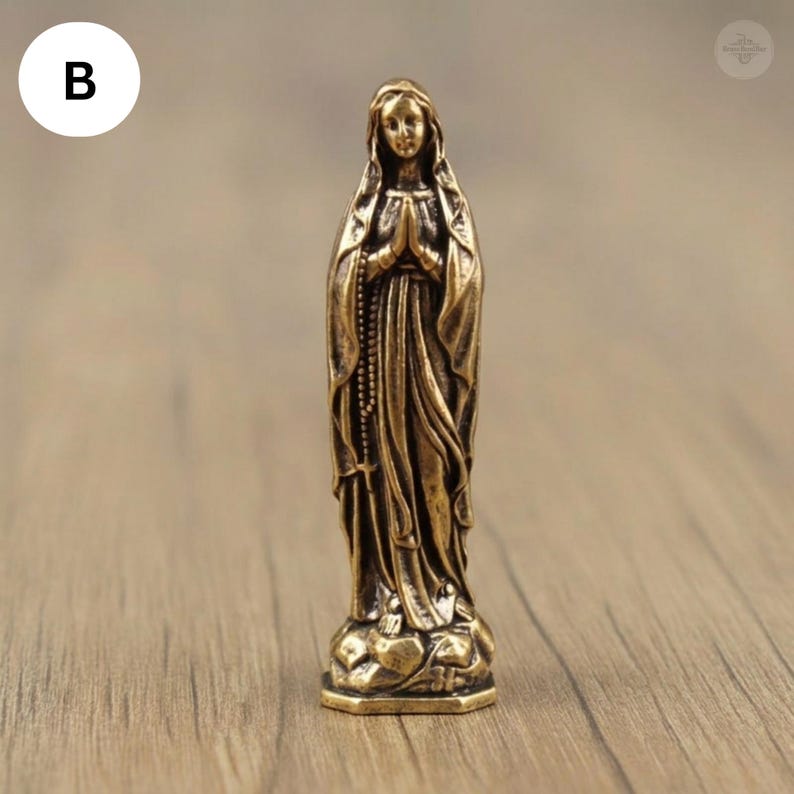Puede incluir: Una peque&ntilde;a estatua de color bronce de una mujer con una t&uacute;nica fluida, con las manos juntas en oraci&oacute;n. La estatua tiene un dise&ntilde;o detallado, incluyendo un rosario y una base detallada. La figura est&aacute; sobre una base detallada.