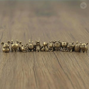 May include: A row of small, bronze-toned figurines representing the Chinese zodiac animals. The set includes a mouse, ox, tiger, rabbit, dragon, snake, horse, sheep, monkey, rooster, dog, and pig. Each figure is intricately detailed.