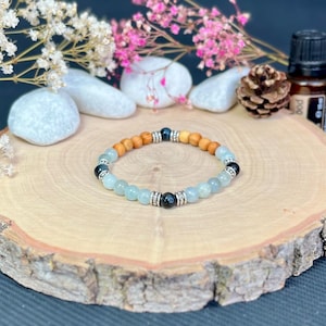 Könnte beinhalten: Ein Perlenarmband bestehend aus einer Kombination von hellblauen, durchscheinenden Perlen, glatten braunen Holzperlen und glänzenden schwarzen Perlen, akzentuiert durch silberfarbene Metallzwischenstücke in einem wiederkehrenden Muster.