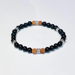 Könnte beinhalten: Schwarzes Perlenarmband mit Lavastein-, Onyx- und Rudraksha-Perlen. Das Armband hat silberfarbene Abstandshalter. Die Perlen sind auf einem elastischen Band aufgefädelt. Ein stilvolles Accessoire.