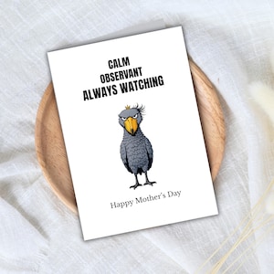 May include: A white greeting card with the text "CALM OBSERVANT ALWAYS WATCHING" and "Happy Mother's Day". The card features a cartoon illustration of a gray bird with a yellow beak and a crown.