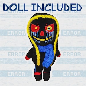 Op de afbeelding: Een handgemaakte gehaakte pop met een zwart lichaam, een geel omrande capuchon en een blauwe sjaal. De pop heeft rode en gele ogen, een gele glimlach en blauwe verticale lijnen op het gezicht. De tekst "DOLL INCLUDED" staat bovenaan.