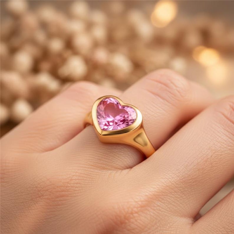 May include: A gold ring featuring a heart-shaped pink gemstone. The ring has a smooth, polished band and a bezel setting that encases the gemstone. The heart-shaped stone is a vibrant pink color.